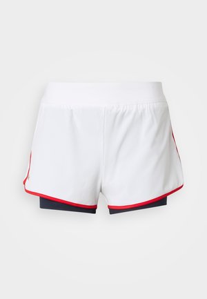 Biele športové šortky s červeným lemom a čiernymi vnútornými kompresnými šortkami viditeľnými pod nimi na jednoliatom pozadí.