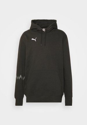 Black hooded sweatshirt made of fabric with a smooth texture. Features a kangaroo pocket, white logo, and chevron pattern on the cuffs.