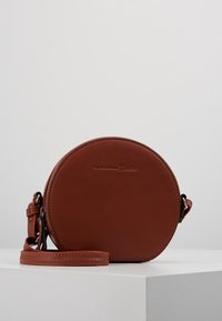 Borsa a tracolla rotonda in pelle marrone con una texture liscia, tracolla regolabile e un logo discreto impresso sul davanti.