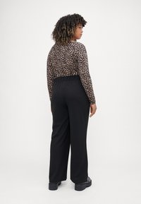 Leopard print long-sleeve top paired with high-waisted black wide-leg trousers. Smooth fabric, elastic waistband, subtle sheen on pants.