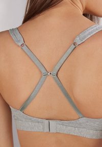 Soutien-gorge gris à texture douce, avec des bretelles croisées réglables et une fermeture à crochet au dos.