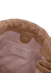 Lichtroze stoffen interieur van een handtas met een bruine leren rand. Beschikt over een label met de tekst "Coccinelle Authentiek Italiaans Leer."