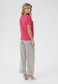 T-shirt fuchsia à manches courtes avec un col rond, associé à un jean large gris clair avec un ourlet effiloché et des poches arrière.