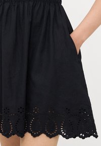 Μαύρη λινή φούστα με πτυχωτή μέση, τσέπες και περίπλοκο σχέδιο δαντέλας με κοπή λέιζερ στην άκρη, διακοσμημένη με λουλούδια.