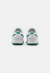 Sapatilhas Nike brancas com acentos verdes, apresentando um cabedal liso, gola almofadada e solas de borracha texturizada. A vista traseira mostra detalhes do logótipo.