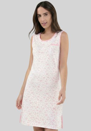 Mujer con vestido blanco sin mangas con estampado floral rosa y ribete rosa, posando frente a un fondo gris liso.