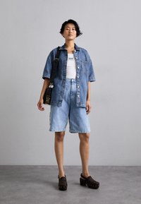 Denim krekls ar īsām piedurknēm, gaiši zili augstās jostas šorti un tumši brūni klogi ar perforētu rakstu un kniedēm. Melna soma ar "LOVE" detaļu.