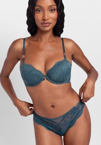 Teal lace bra with padded cups, thin straps, and floral pattern. Matching lace panties feature sheer panels and scalloped edges.