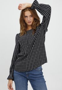 Camicia a maniche lunghe a scacchi bianco e nero con scollatura quadrata e maniche arricciate, abbinata a jeans blu. Tessuto liscio e leggero.