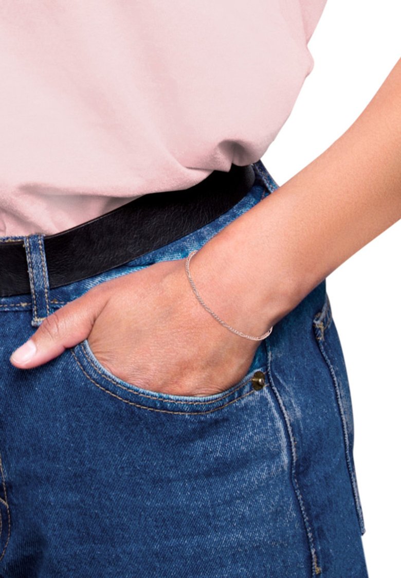 Silver kedjearmband bärs på en hand, med en ljusrosa skjorta och högmidjade blå jeans. Närbild på armbandets detaljer.