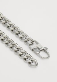 Silver metal chain featuring oval links with a polished finish. Includes a clasp with engraved detailing for secure closure.