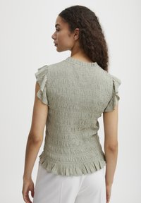 Haut ajust�é vert clair en tissu texturé, avec des manches courtes à volants et un ourlet froncé. Présente un design froncé sur l'ensemble du corps.