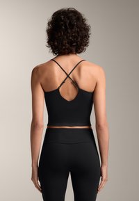 Fekete sportos crop top V-alakú hátrésszel, keresztezett pántokkal és texturált derékrésszel, fekete, magas derekú leggings-szel párosítva.