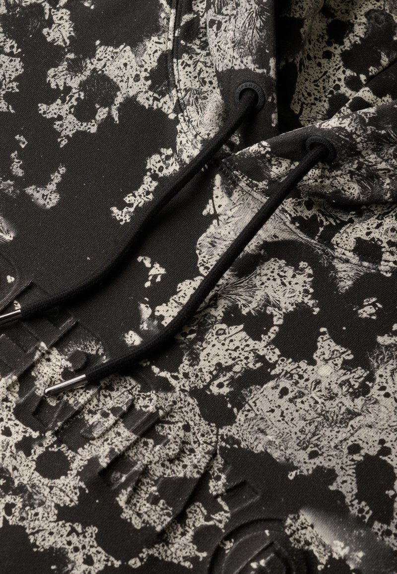 Czarna bluza z kapturem z teksturowanym, plamkowym wzorem w odcieniach szarości. Posiada czarne sznureczki z metalowymi, srebrnymi końcówkami oraz wytłoczone litery na materiale.