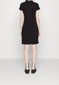 Robe noire à manches courtes avec une silhouette ajustée, longueur genoux, associée à des bottines beiges à chevilles avec des accents noirs et une semelle épaisse.