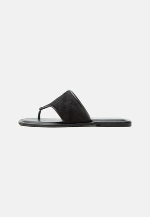 Svart flat sandal med bred teksturert stropp og tåslynge, vist fra siden på enkel lys bakgrunn.