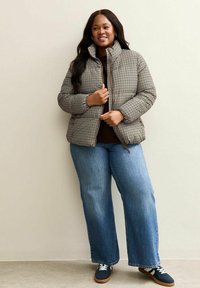 Giacca trapuntata a scacchi in marrone e crema, con colletto alto. Abbinata a jeans a gamba dritta blu e scarpe navy con lacci bianchi.