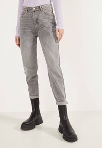 Jeans de denim gris de cintura alta con un corte recto, detalles desgastados y dobladillos ajustados, combinados con botas negras de plataforma gruesa.