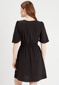 Vestito nero a maniche corte con vita arricciata, dalla superficie liscia e dalla vestibilità comoda. La parte posteriore presenta un sottile design a coste.