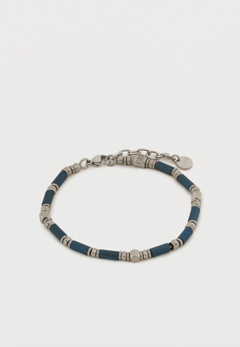 Ασημένιο και σκούρο μπλε βραχιόλι με χάντρες, με κούμπωμα αστακού και μικρή στρογγυλή ετικέτα μάρκας σε λευκό φόντο.