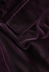 Samtstoff in tiefem Lila mit einer glatten, weichen Textur. Verfügt über einen subtilen Glanz und Falten, die Tiefe und Dimension erzeugen.
