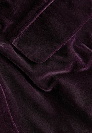 Samtstoff in tiefem Lila mit einer glatten, weichen Textur. Verfügt über einen subtilen Glanz und Falten, die Tiefe und Dimension erzeugen.