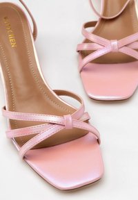 Roze sandaaltjes met bandjes en een vierkante neus. Gemaakt van glanzend synthetisch materiaal, met kruisende bandjes en een soepele beige binnenzool.