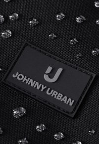 Tessuto nero strutturato con gocce d'acqua e un'etichetta rettangolare nera con testo in rilievo "JOHNNY URBAN" e un logo J stilizzato.