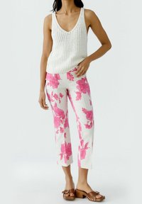 Débardeur blanc en tricot avec un col en V, associé à un pantalon court rose à motif floral et des sandales à talons carrés marron.