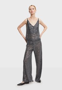 Strieborný top so sequínmi a široké nohavice s výstrihom do V a tenkými ramienkami. Hladká textúra s reflexným povrchom. Nosené čierne baleríny.