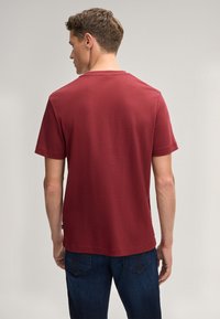 Bordeauxfarbener Baumwoll-T-Shirt mit Kurzarm und Rundhalsausschnitt, mit geradem Saum. Glatte Textur, keine sichtbaren Muster oder Grafiken.