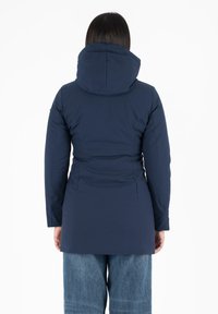 Veste isolante bleu marine avec capuche, coupe slim et manches longues. Présente une taille froncée et une texture de tissu lisse.