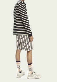 Gestreiftes Langarmoberteil in Marineblau und Creme, gestreifte Shorts in Creme und Dunkelbraun, gestreifte Socken und grau-weiße Sneaker.