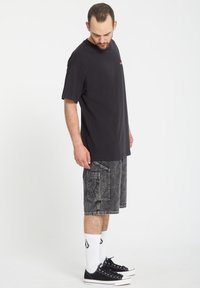 T-shirt en coton noir à manches courtes et col rond, associé à un short en jean gris avec une poche plaquée. Baskets noires et chaussettes blanches.