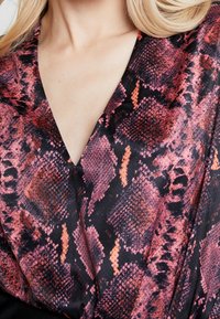 Schwarzer Stoff mit pink-orangenen Schlangenmuster, ausgestattet mit einem tiefen V-Ausschnitt und einer glatten Textur.