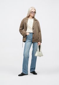 Brown outer jacket with large buttons, cream top, blue flared jeans, black shoes, and a small light gray handbag. Long straight hair.