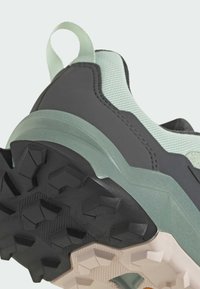 Zapatilla con una parte superior texturizada en verde menta y acentos en gris oscuro, diseñada con una suela de goma negra resistente para ofrecer tracción y estabilidad.
