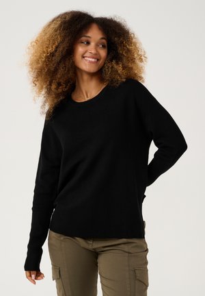 Black ribbed sweater with a relaxed fit, featuring long sleeves and a wide neckline, paired with khaki cargo pants. Smooth texture, casual design.