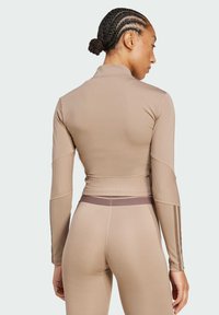 Top atletico beige aderente con maniche lunghe, pannelli laterali a costine e colletto alto. Abbinato a leggings coordinati con un accento sottile.