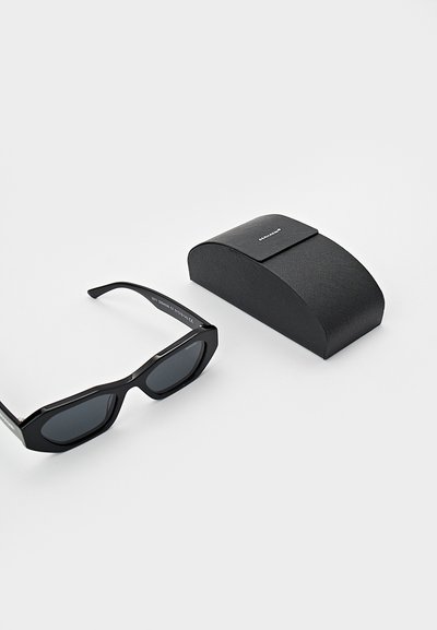 Black sunglasses with an octagonal frame and tinted lenses, paired with a textured black hard case featuring a flap closure.