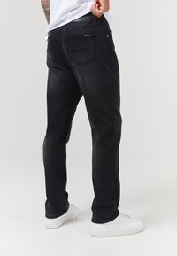 Jeans de mezclilla negra con corte recto, que cuentan con dos bolsillos traseros y una cinturilla simple. Se usan con zapatillas blancas.