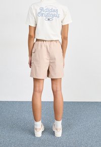 Shorts rosa chiaro con un elastico in vita e due tasche laterali, abbinati a una t-shirt crema con testo grafico blu sulla parte posteriore.