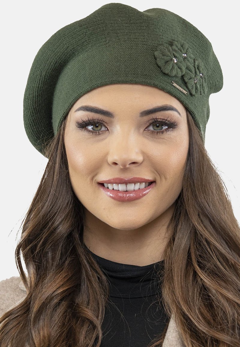 Zöld kötött beret, texturált anyaggal, díszített virágmotívumokkal, amelyekben cirkónia kövek találhatók, valamint egy kis márkacímkével az oldalon.