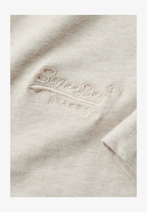 Tessuto di cotone beige chiaro con una consistenza morbida, caratterizzato da un logo ricamato "SuperDry" in un filo di beige leggermente più scuro.