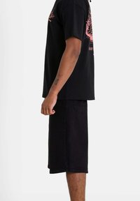 Camiseta de algodón negra de manga corta, con un estampado gráfico en color rosa. Combinada con pantalones cortos de mezclilla negros, de longitud hasta la rodilla, con detalles en el bolsillo trasero.