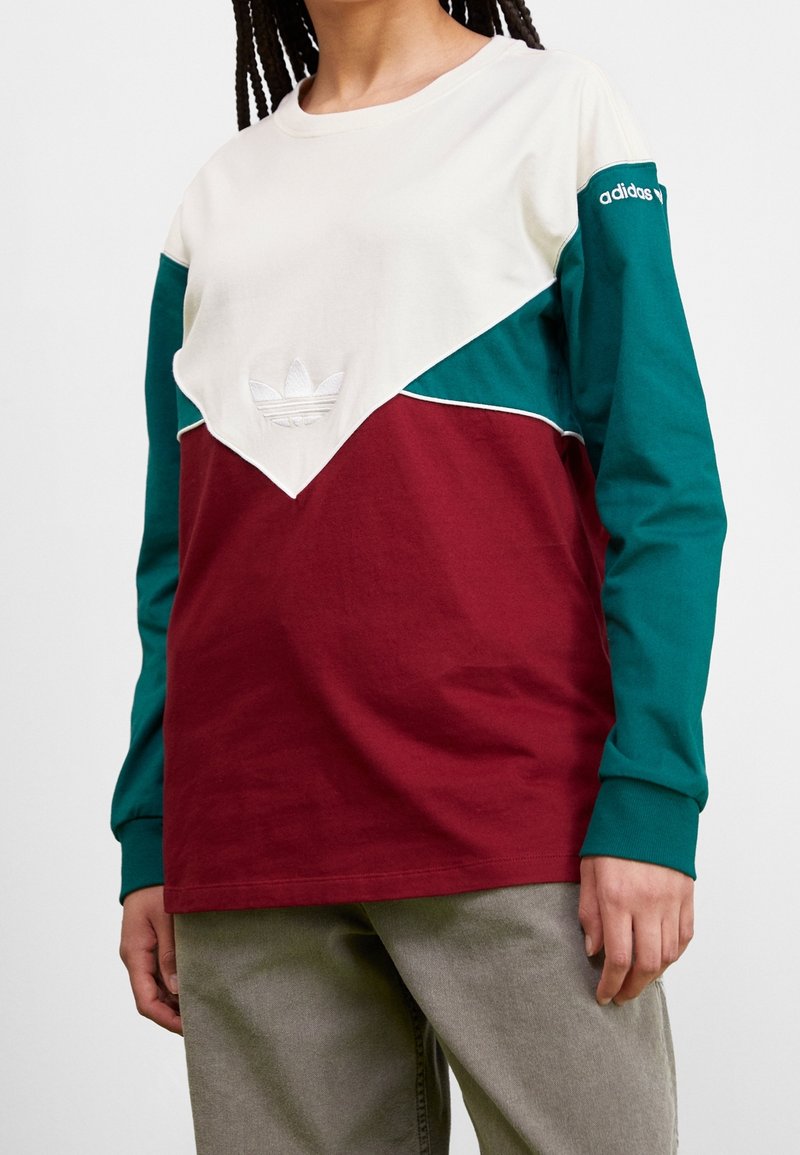 Långärmad skjorta med en krämfärgad kropp, vinröda och teal accenter, med en broderad logotyp och kontrasterande färgade ärmar.