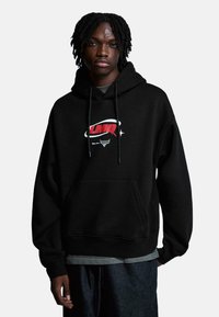 Čierna mikina s kapucňou vyrobená z mäkkej tkaniny s prednou vreckom, ozdobená bielym a červeným grafickým logom, s kapucňou na šnúrku a uvoľneným strihom.