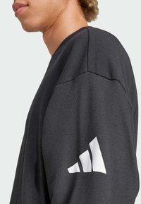 Mørkegrå sweatshirt lavet af bomuldsblanding. Har en rund halsudskæring og et hvidt logo med tre striber på venstre ærme.