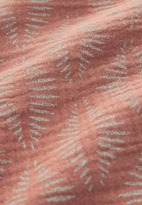 Textile de couleur rose corail avec un motif répétitif de feuilles de fougère blanches. Texture douce avec une apparence légèrement tissée.