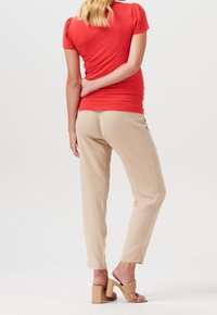 Top rosso aderente con maniche a palloncino corte, abbinato a pantaloni beige a sigaretta. Sandali con tacco a blocco color nocciola completano l'outfit.